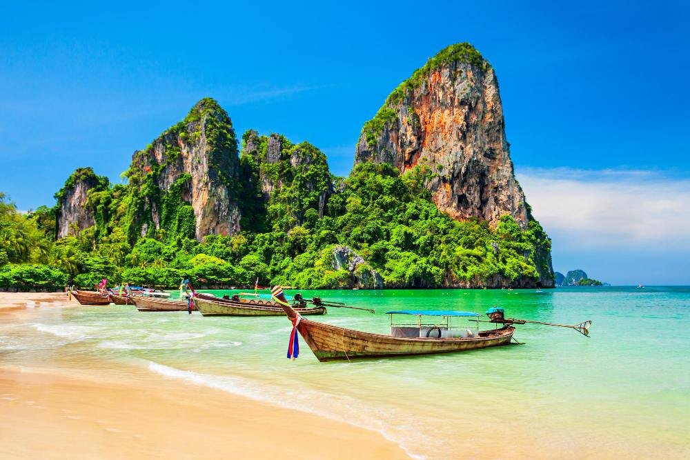 Longtail boats drawn up on the sand below limestone cliffs, waiting to run the Railay crossing